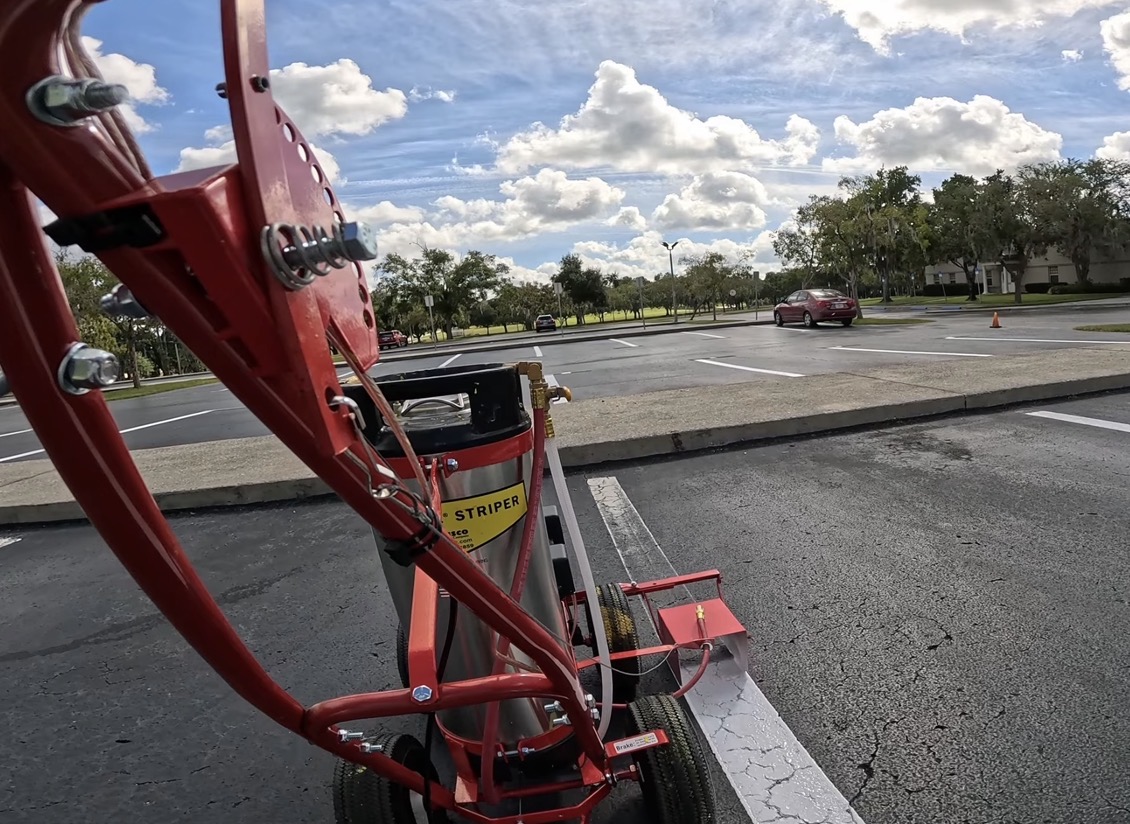 Walk-behind striping machine following an existing white parking-space line